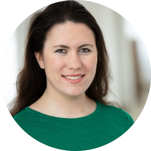Woman with long dark hair wearing a green top, smiling at the camera against a softly blurred background.
