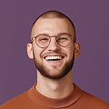 Smiling young man with glasses and a beard against a purple background.