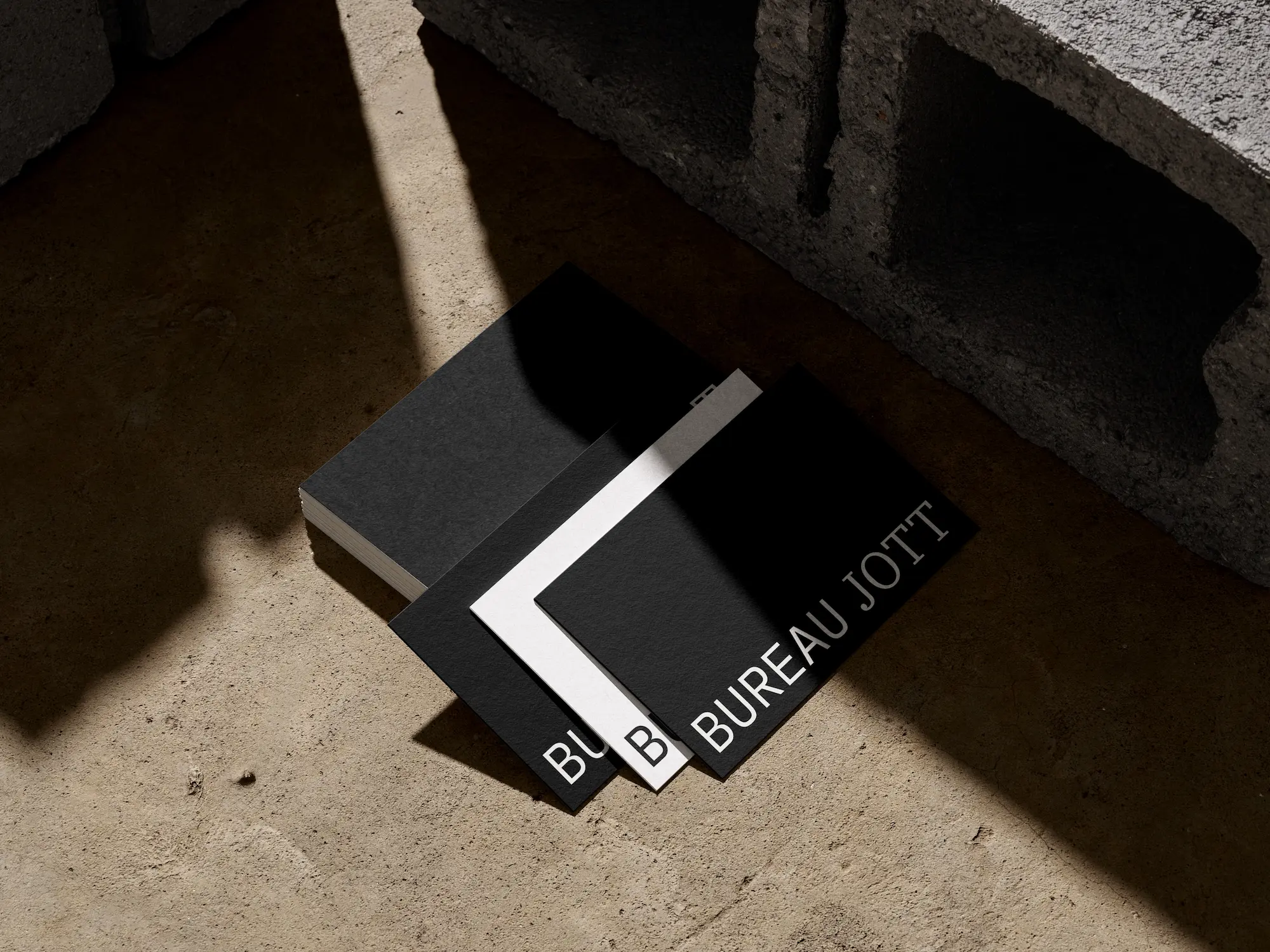 Drei minimalistische Visitenkarten mit dem Text 'BUREAU JOTT' auf einem Betonboden mit Schatten.