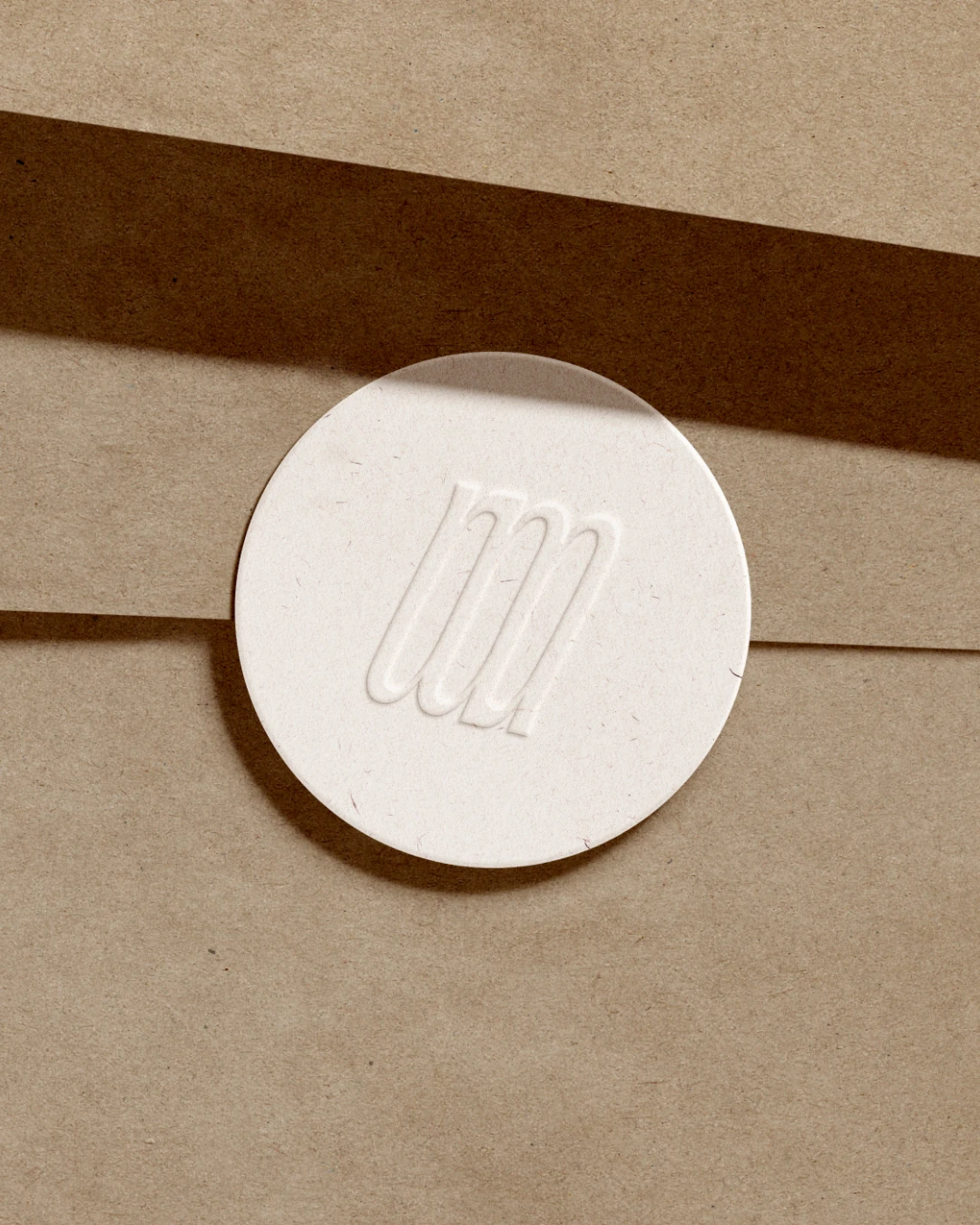 Weißer runder Siegelstempel mit eingraviertem Monogramm auf braunem Papier mit Schatten.