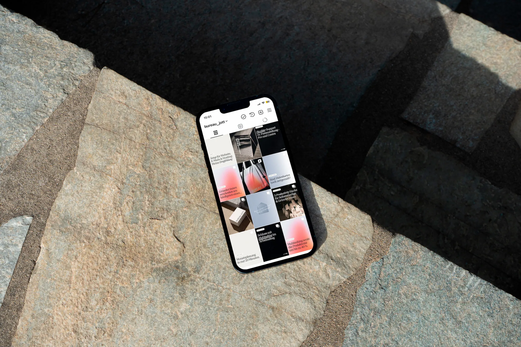 Smartphone zeigt ein Instagram-Profil mit unterschiedlichen Beiträgen auf einem Pflastersteinboden.
