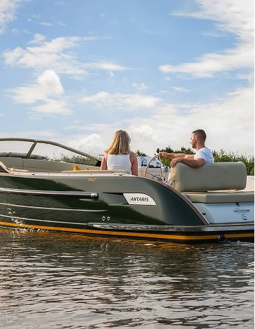 Twee personen zitten op een ANTARIS boot rustig op het water met een blauw bewolkte hemel.