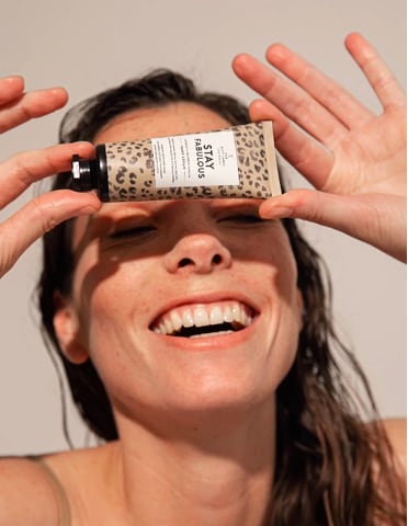Vrouw met nat haar lacht en houdt een tube Stix Sabljouos huidcrème boven haar ogen.