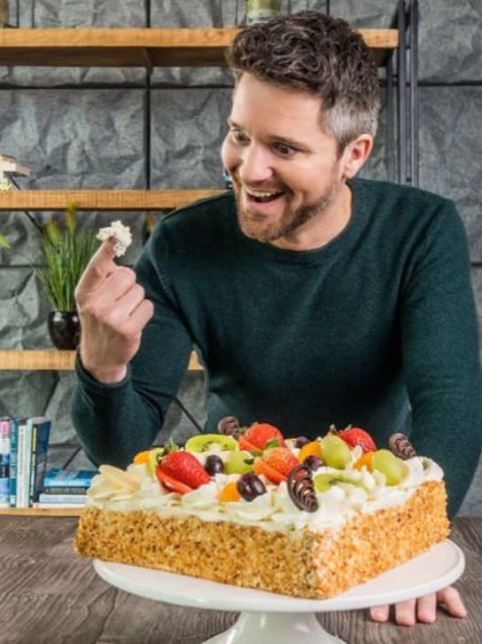 Man geniet verrast van een stuk fruitige slagroomtaart op een houten tafel.