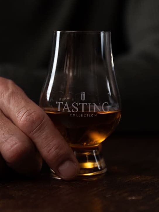 Hand die een Whisky Tasting Collection-glas met amberkleurige whisky vasthoudt.