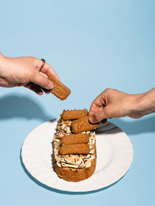 Twee handen plaatsen koekjes op een dessert met room en gehakte noten op een wit bord.