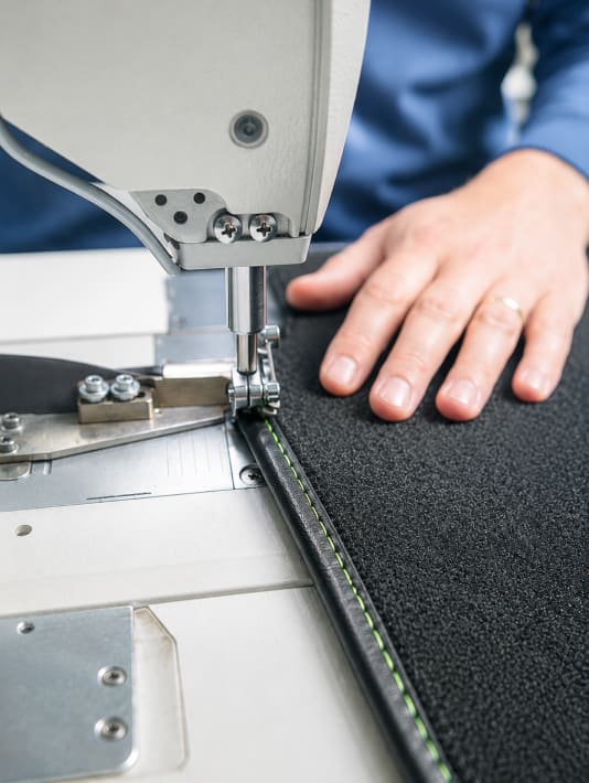 Een hand naait een zwarte stof met een groene stiklijn op een naaimachine.