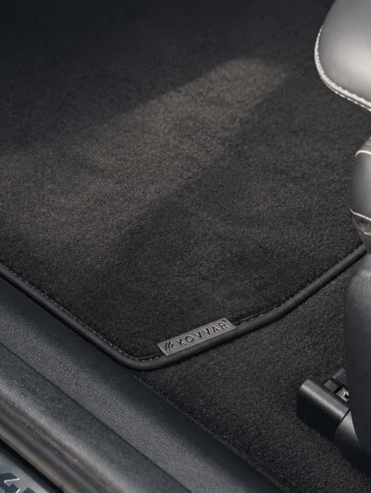 Zwarte autovloermat met Kovvar-label naast een autostoel met stiknaden.