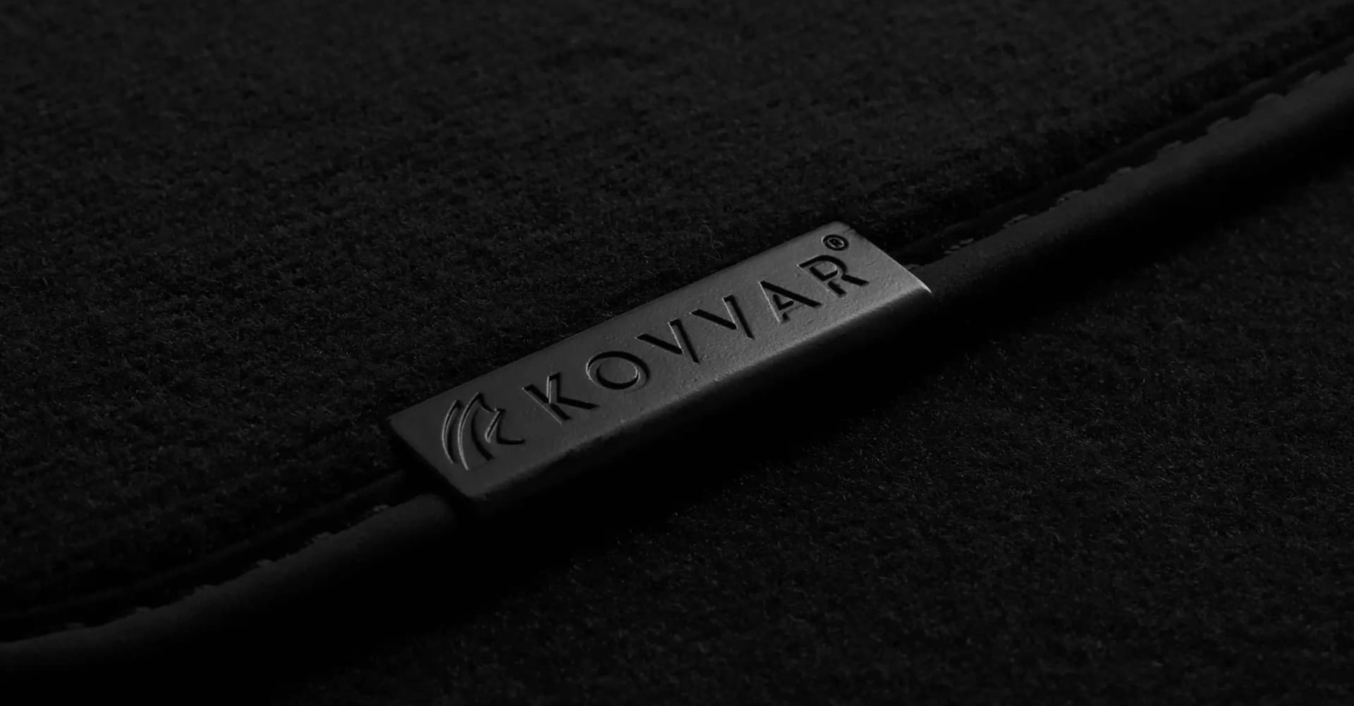 Zwarte metalen label met daarop de tekst KOVVAR op donkere stof.