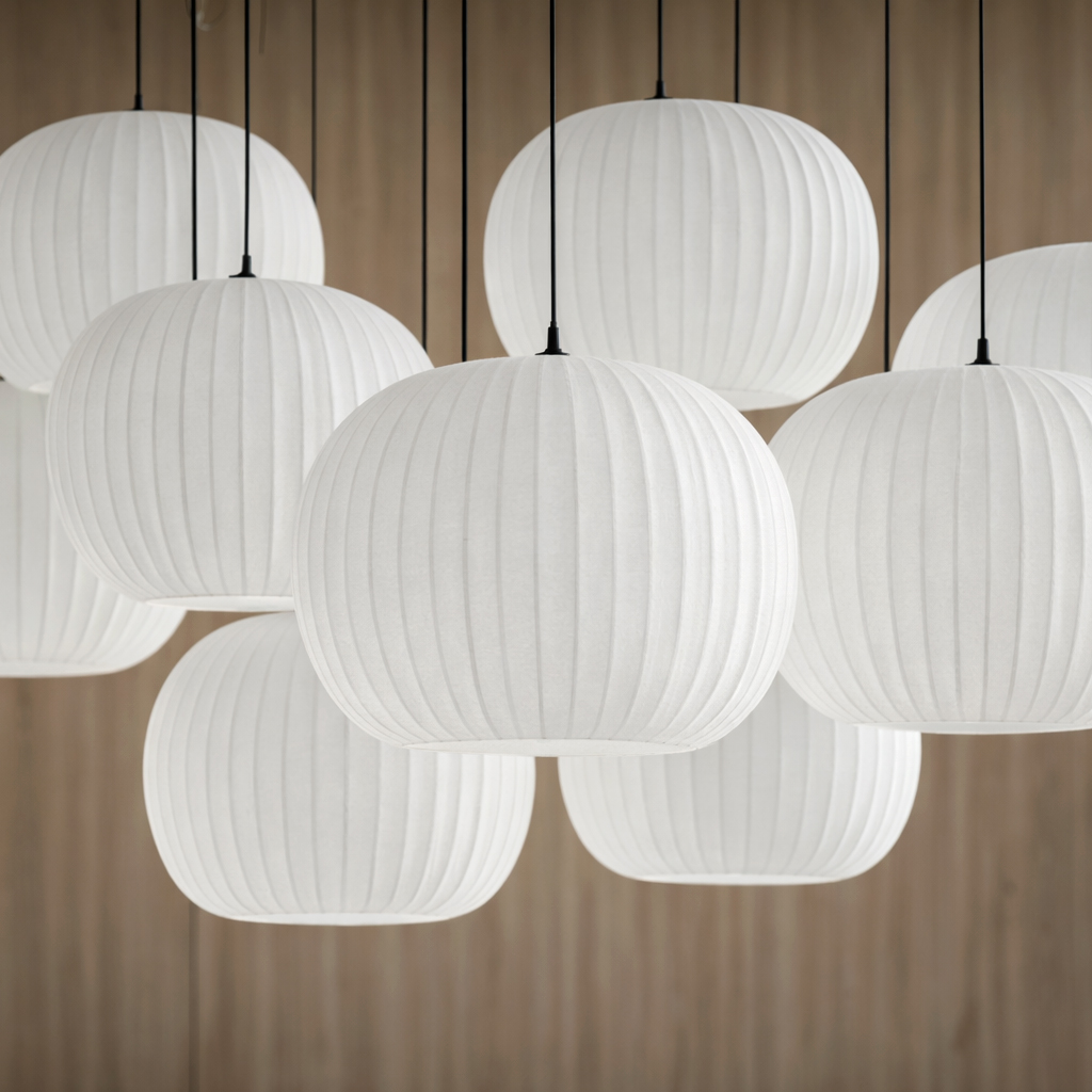 A tight shot of several white, ribbed, globe-shaped pendant lamps suspended by thin black cords against a warm wood background.