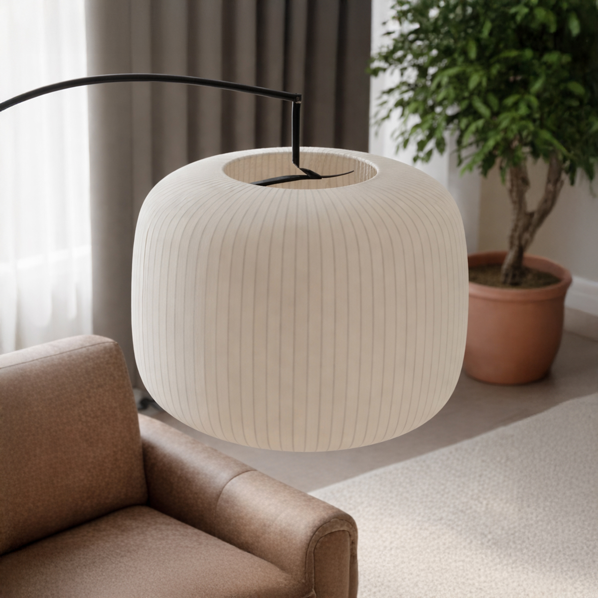 A close-up, eye-level shot of a large, cream-colored, pleated drum lampshade. The shade is suspended from a thin black arched arm in a modern living room setting.