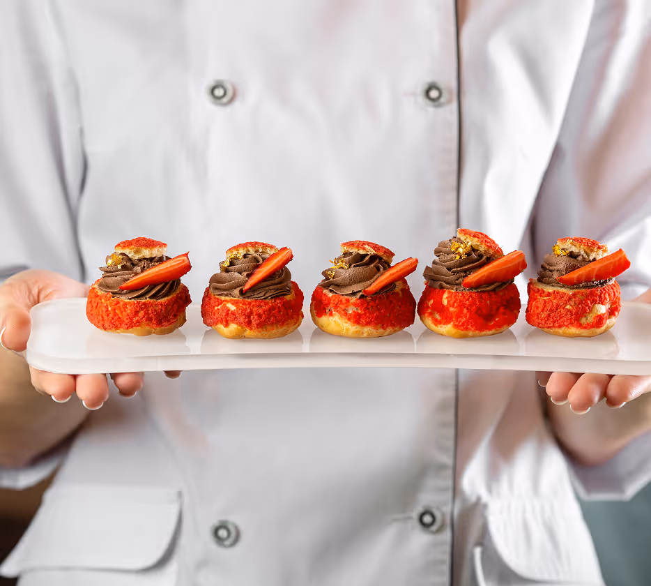 Chef hält ein Tablett mit kleinen Dessertgebäcken, gefüllt mit Schokoladencreme und dekoriert mit frischen Erdbeeren.