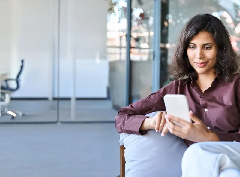 A woman sitting in a chair looking at a mobile phone.