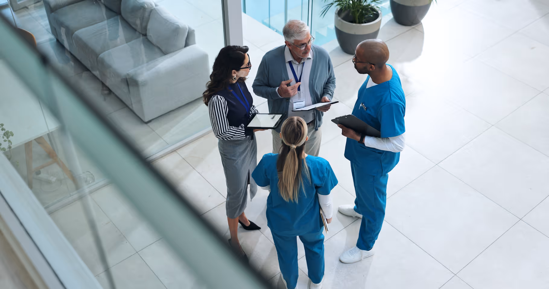 Älterer Mann und drei medizinische Fachkräfte in Besprechung in modernen Krankenhausflur.