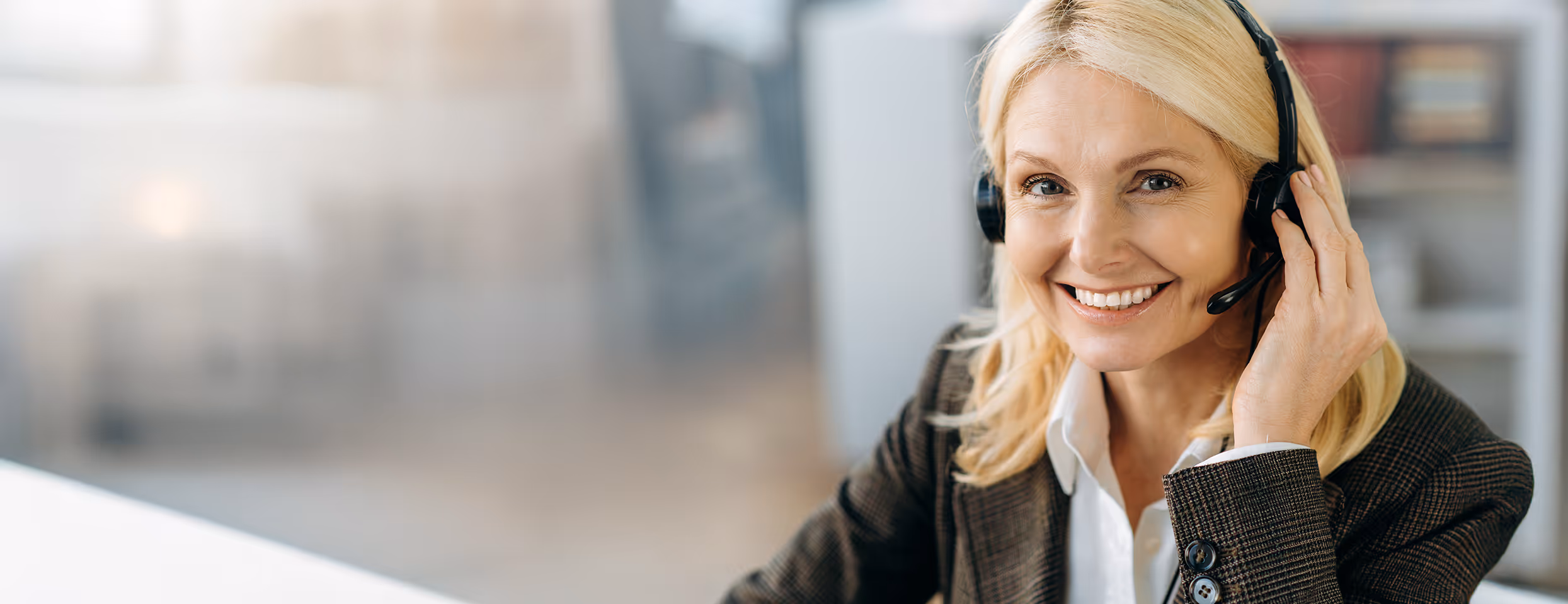 Lächelnde blonde Frau in Businesskleidung mit Headset, die einen Kundendienst oder Support anbietet.