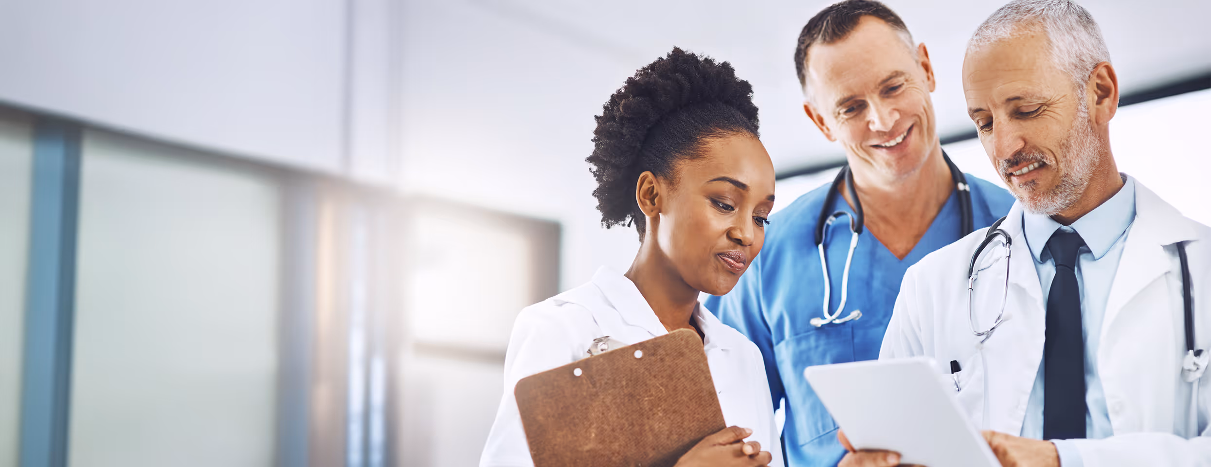 Drei Ärztinnen und Ärzte, eine Frau mit Klemmbrett und zwei Männer mit Stethoskopen, die sich ein Tablet ansehen.