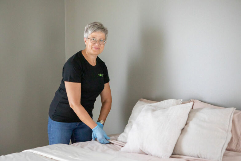 Iloinen henkilö petaamassa vaaleasävyistä sänkyä.