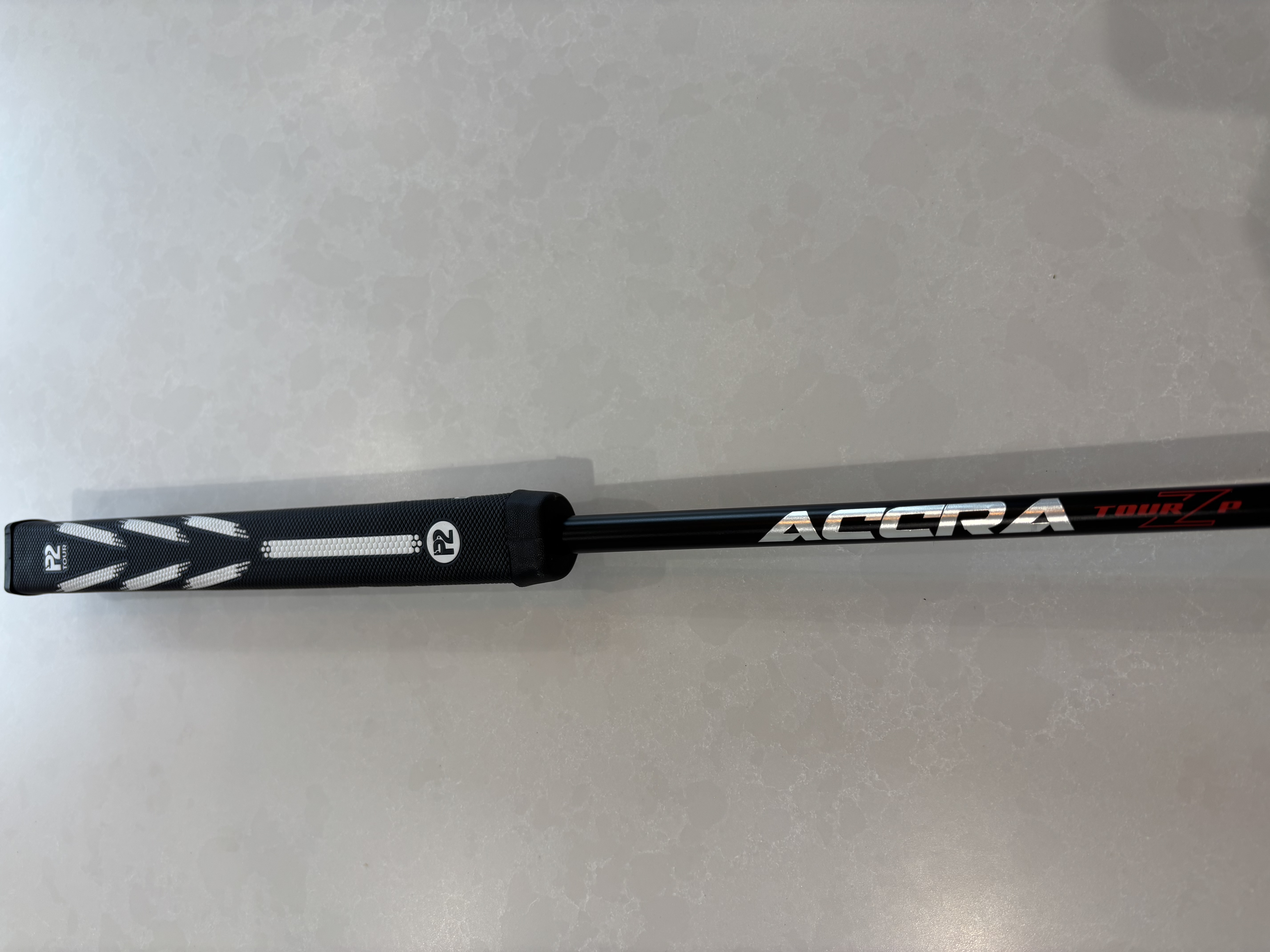 Black golf club grip reading P2 Tour with Acura logo on the shaft on a grey surface.