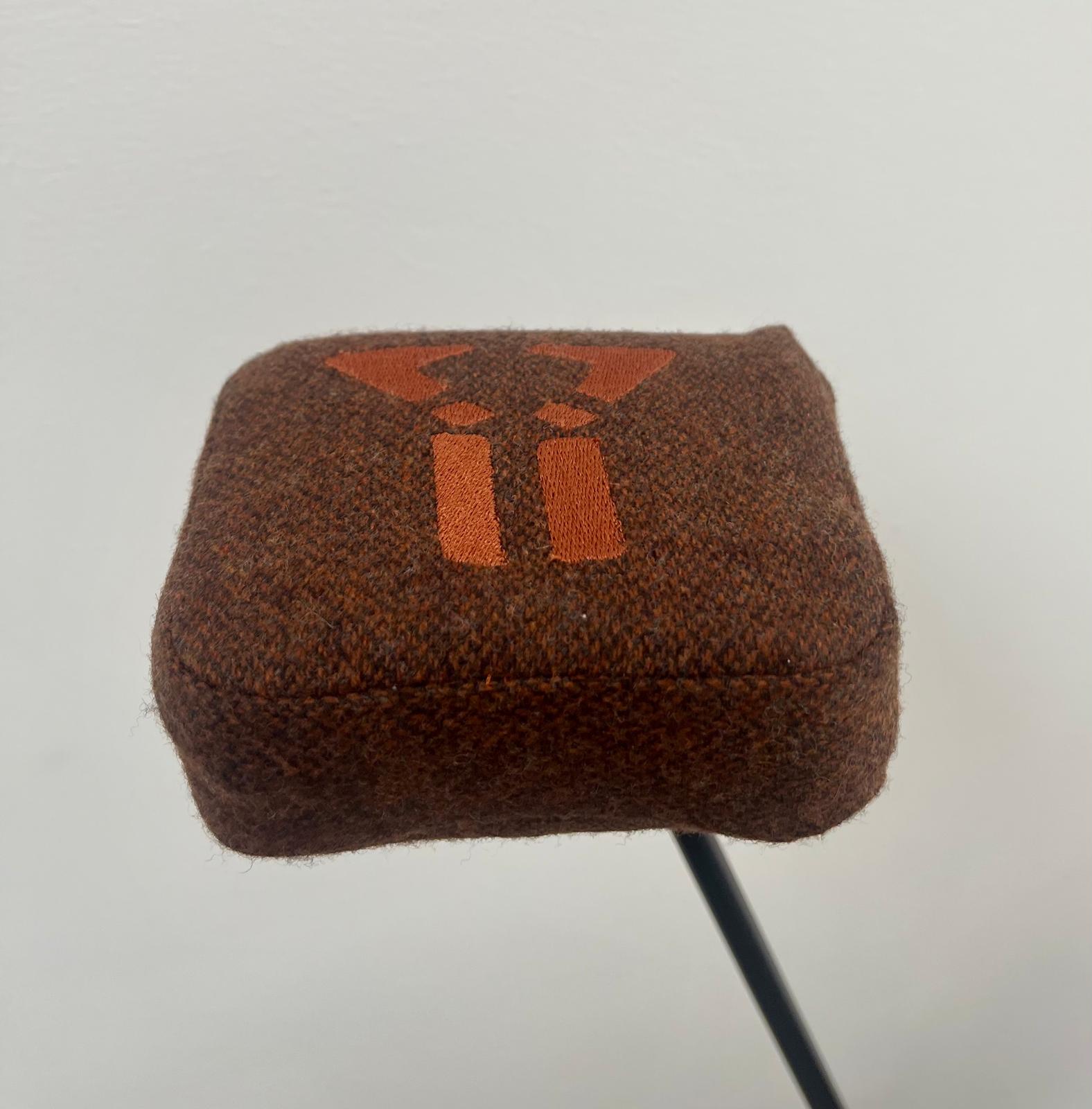 Brown fabric golf club headcover with an orange geometric design on top.
