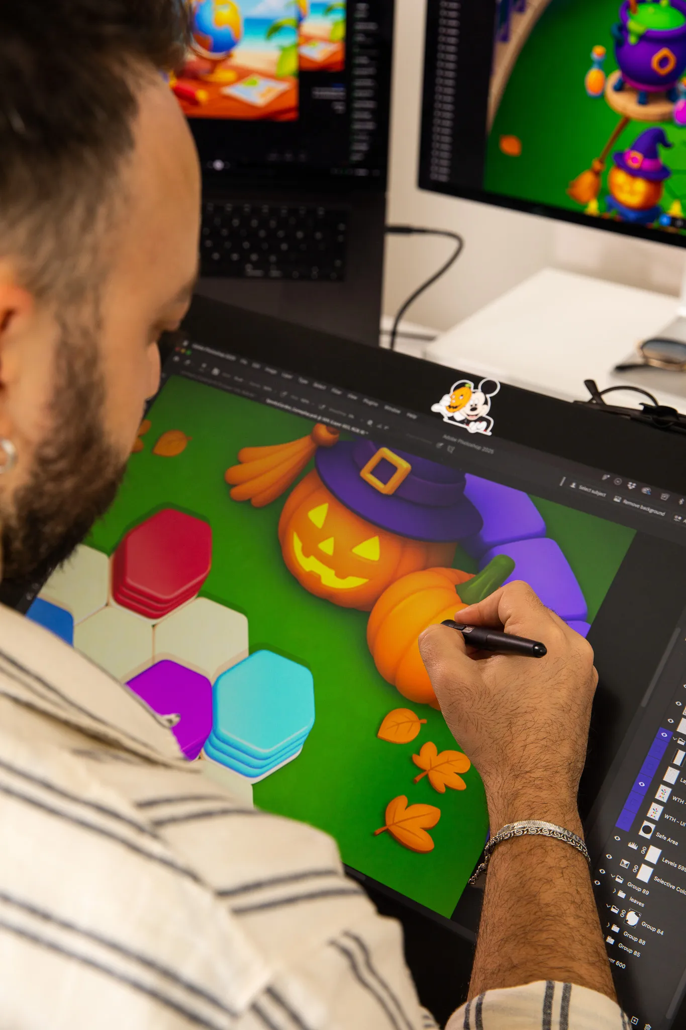 Man using a stylus on a graphic tablet to create a digital artwork featuring Halloween pumpkins and colorful hexagonal shapes.