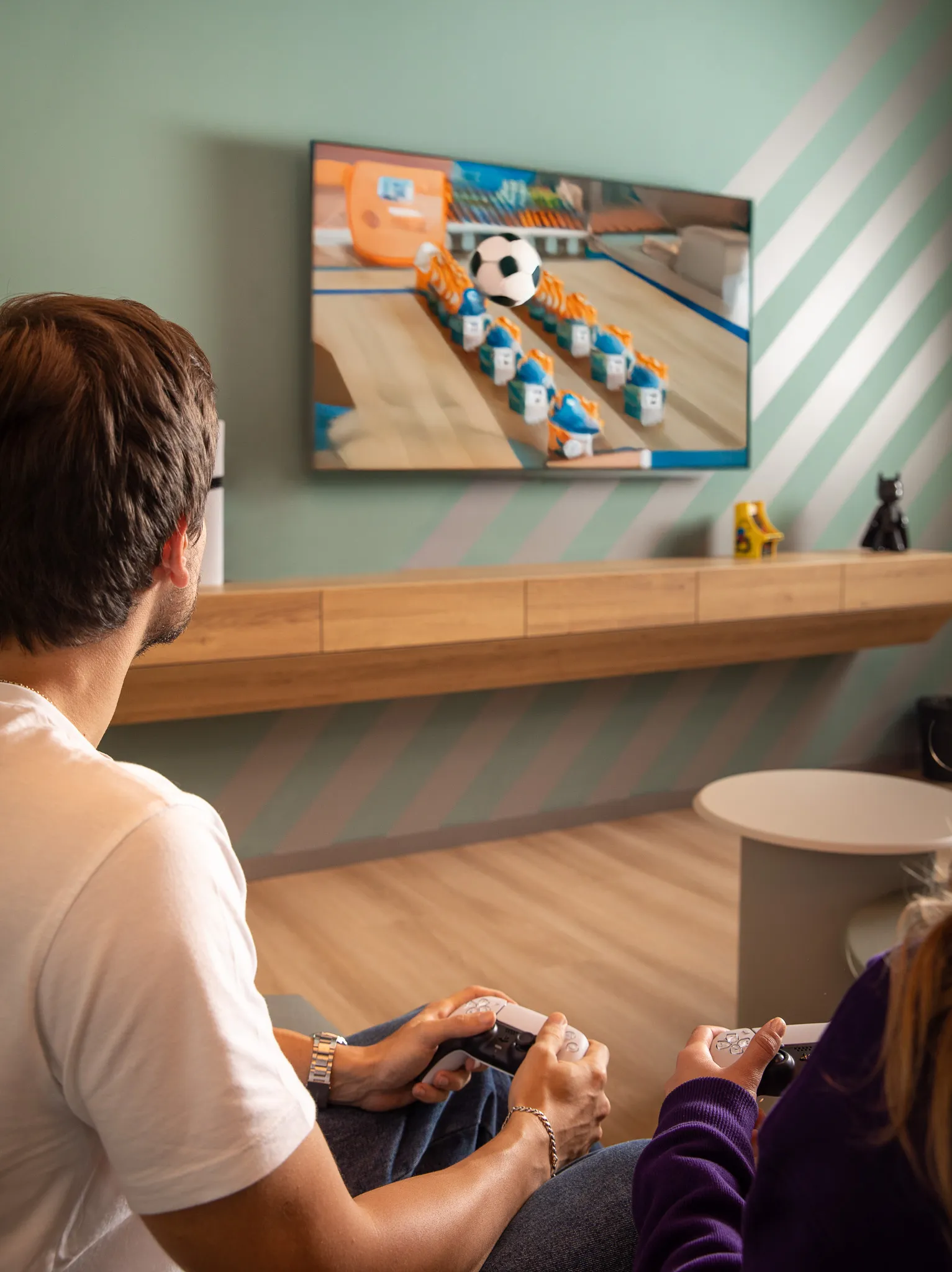 Two people sitting on a couch playing a soccer-themed video game with game controllers.