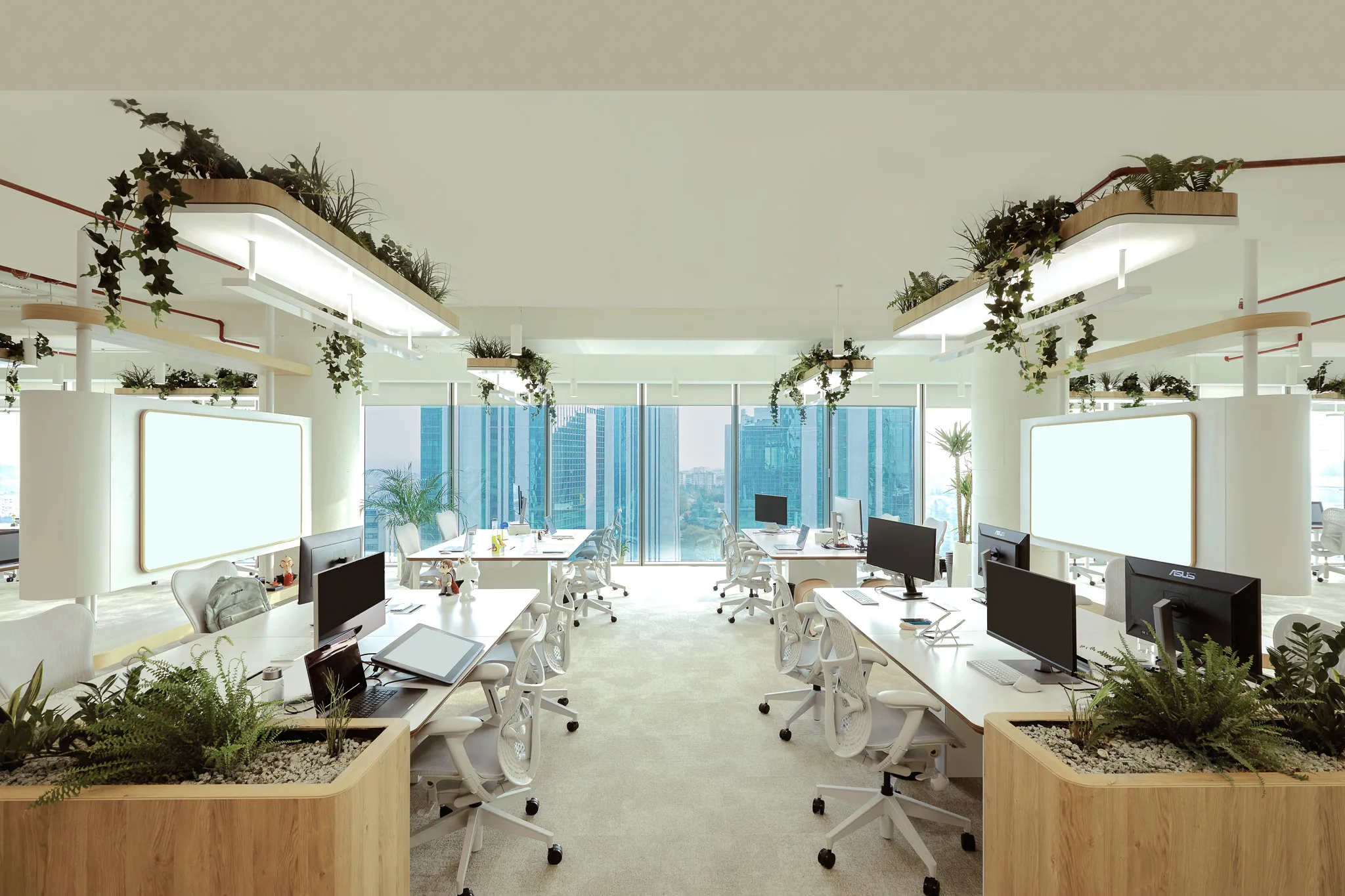 Bright modern office space with white desks, ergonomic chairs, multiple computer monitors, and hanging planters with green plants, overlooking city skyscrapers through large windows.