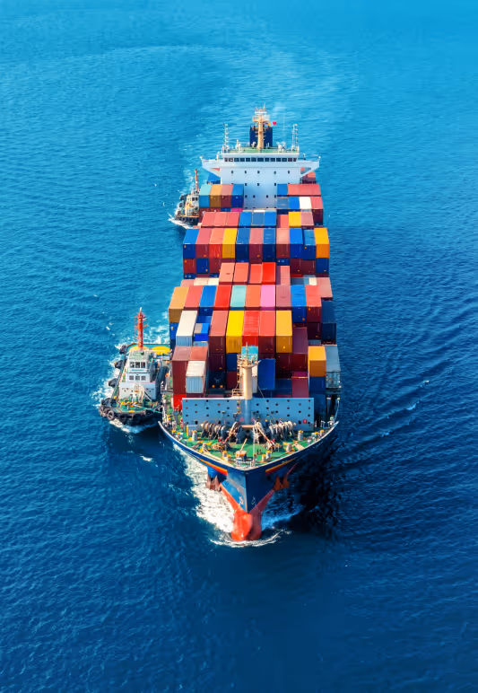 Container ship loaded with colorful shipping containers sailing on blue ocean accompanied by a small tugboat.