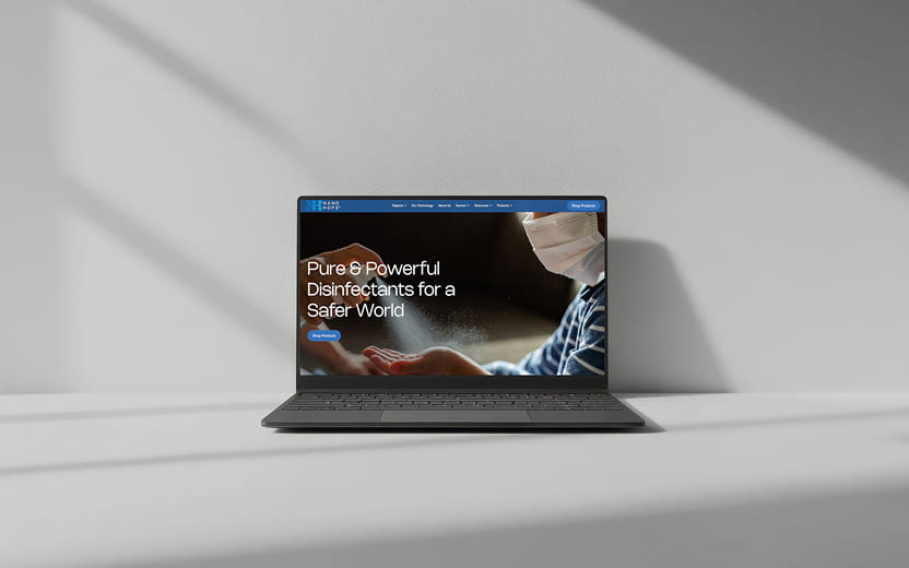 Open laptop on a table displaying a website with a person wearing a mask and spraying disinfectant, captioned 'Pure & Powerful Disinfectants for a Safer World.'
