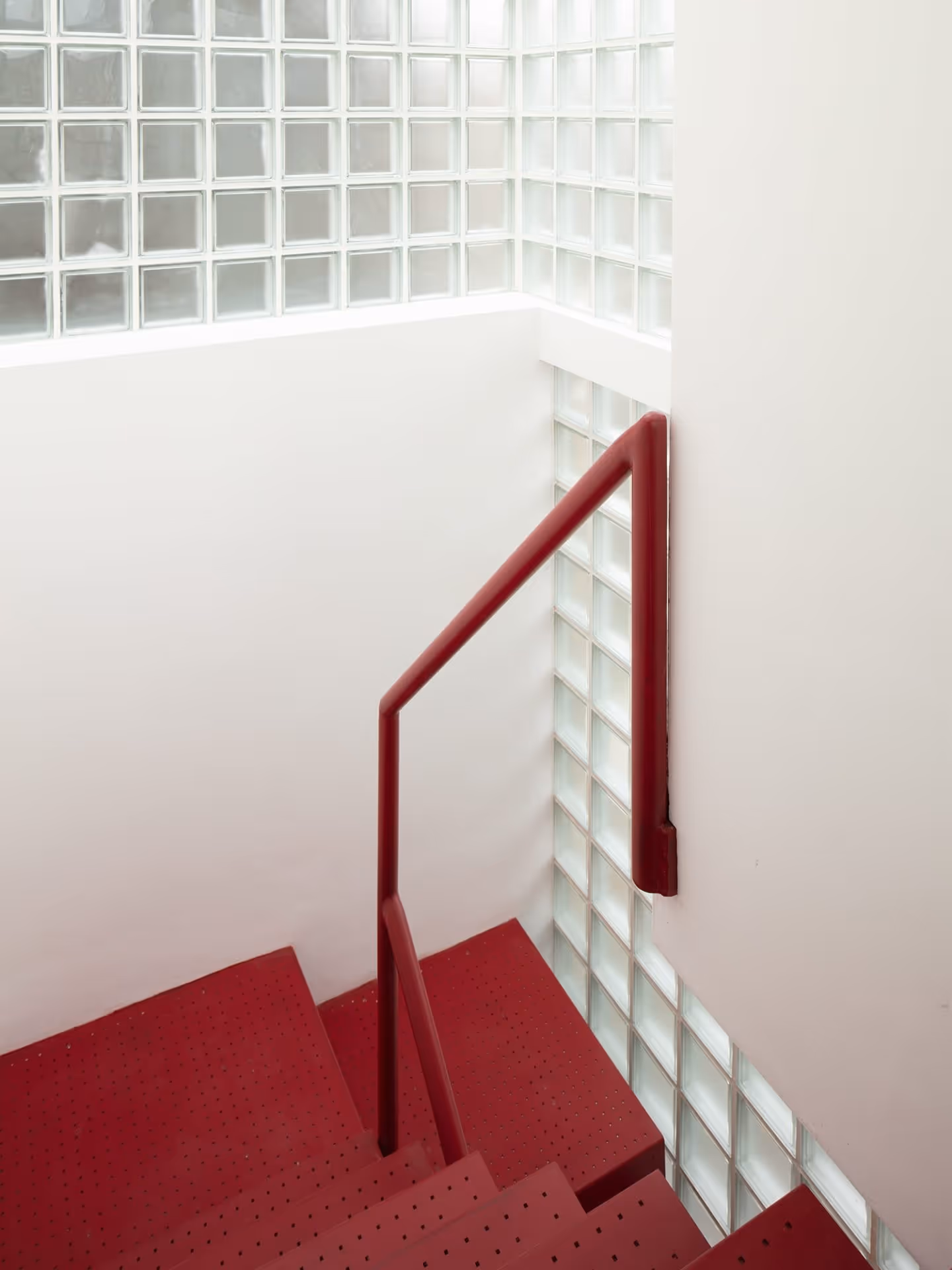 MARYLAND HOUSE | A striking deep red staircase at Maryland House, framed by glass block walls that flood the space with natural light, exemplifying the inventive use of vertical circulation and daylight in infill housing architecture.