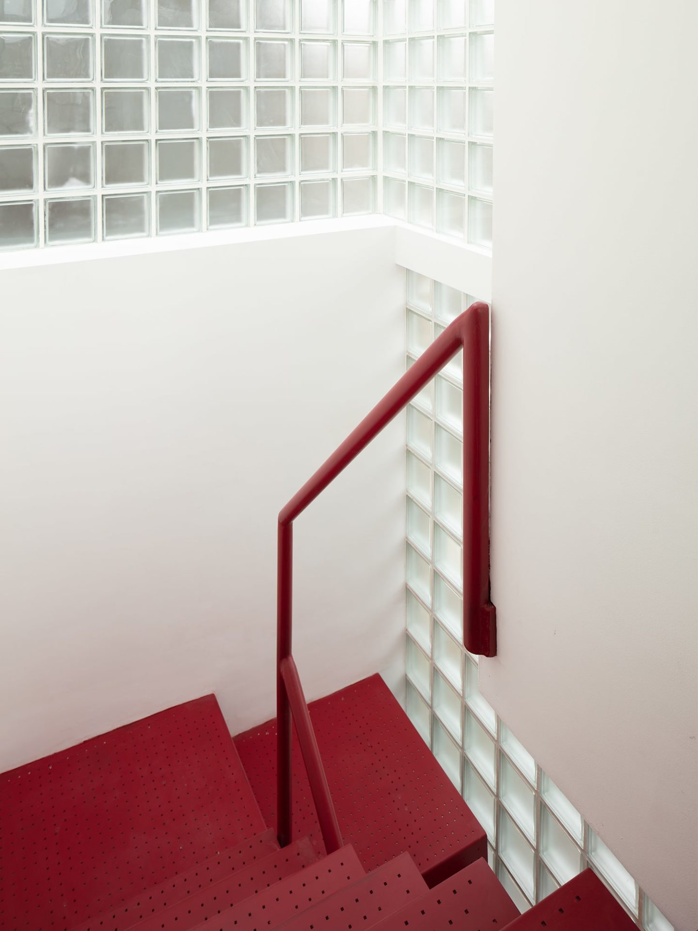 MARYLAND HOUSE | A striking deep red staircase at Maryland House, framed by glass block walls that flood the space with natural light, exemplifying the inventive use of vertical circulation and daylight in infill housing architecture.