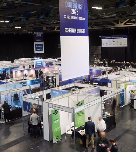 Large indoor exhibition hall with multiple vendor booths and people walking and talking at the Event Production and Exhibition conference.