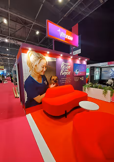 Trade show booth with red seating, a circular white table, and a large banner showing a woman working and text about purpose-driven business.