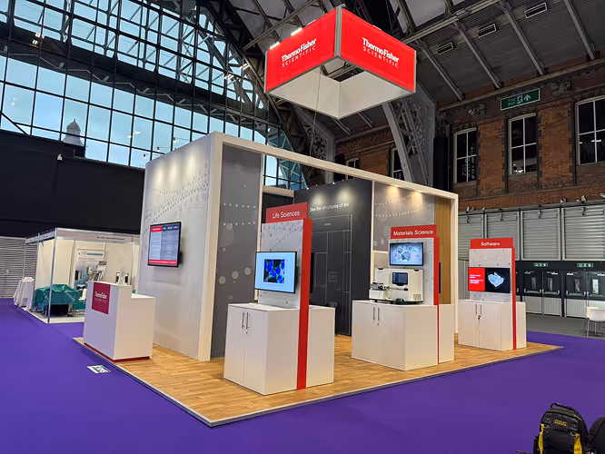 Thermo Fisher Scientific exhibition booth with displays for Life Sciences, Materials Science, and Software in a large industrial hall with purple flooring.