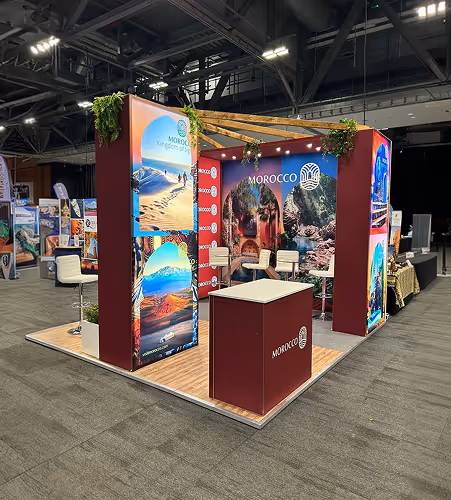 Morocco-themed exhibition booth with scenic posters of landscapes, desert, mountains, and cultural sites, featuring chairs and a reception desk.