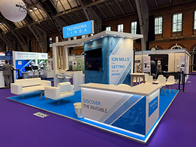 Technoorg exhibition booth with blue and white design, seating area, and displays at a trade show.