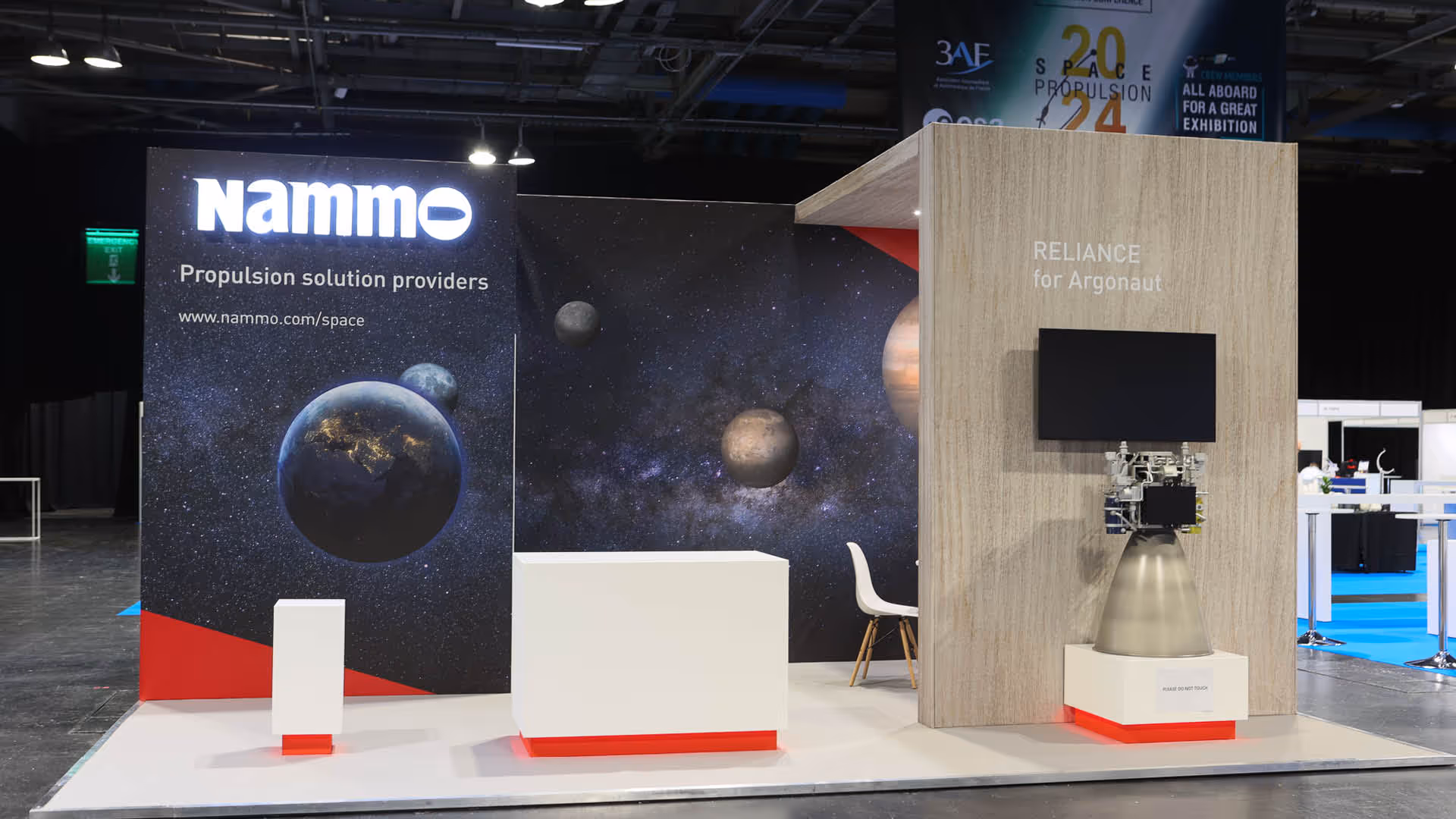 Nammo exhibition booth with space-themed backdrop, Earth and planets images, and rocket engine display labelled 'RELIANCE for Argonaut'.