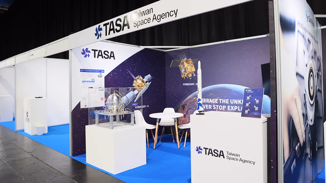 Exhibition booth of Taiwan Space Agency with satellite models, a round table with chairs, and space-themed backdrop.