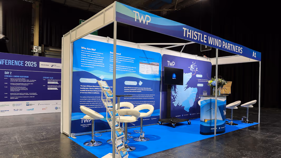 Thistle Wind Partners exhibition booth with blue-themed panels, white chairs, a tall brochure stand, and a screen displaying a map.