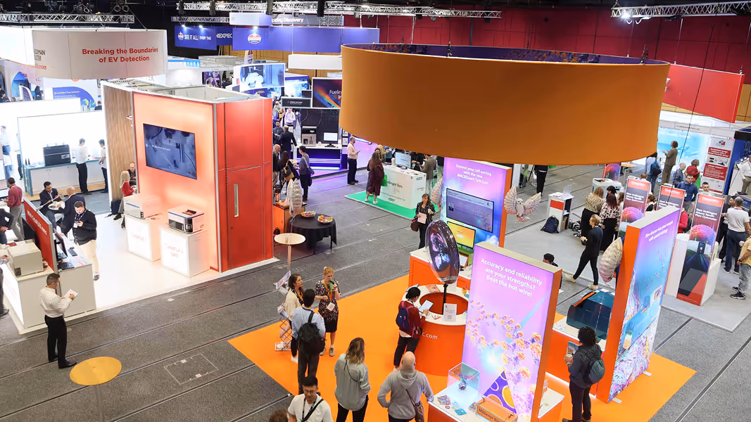 Busy technology exhibition with various brightly lit booths and attendees interacting around displays.
