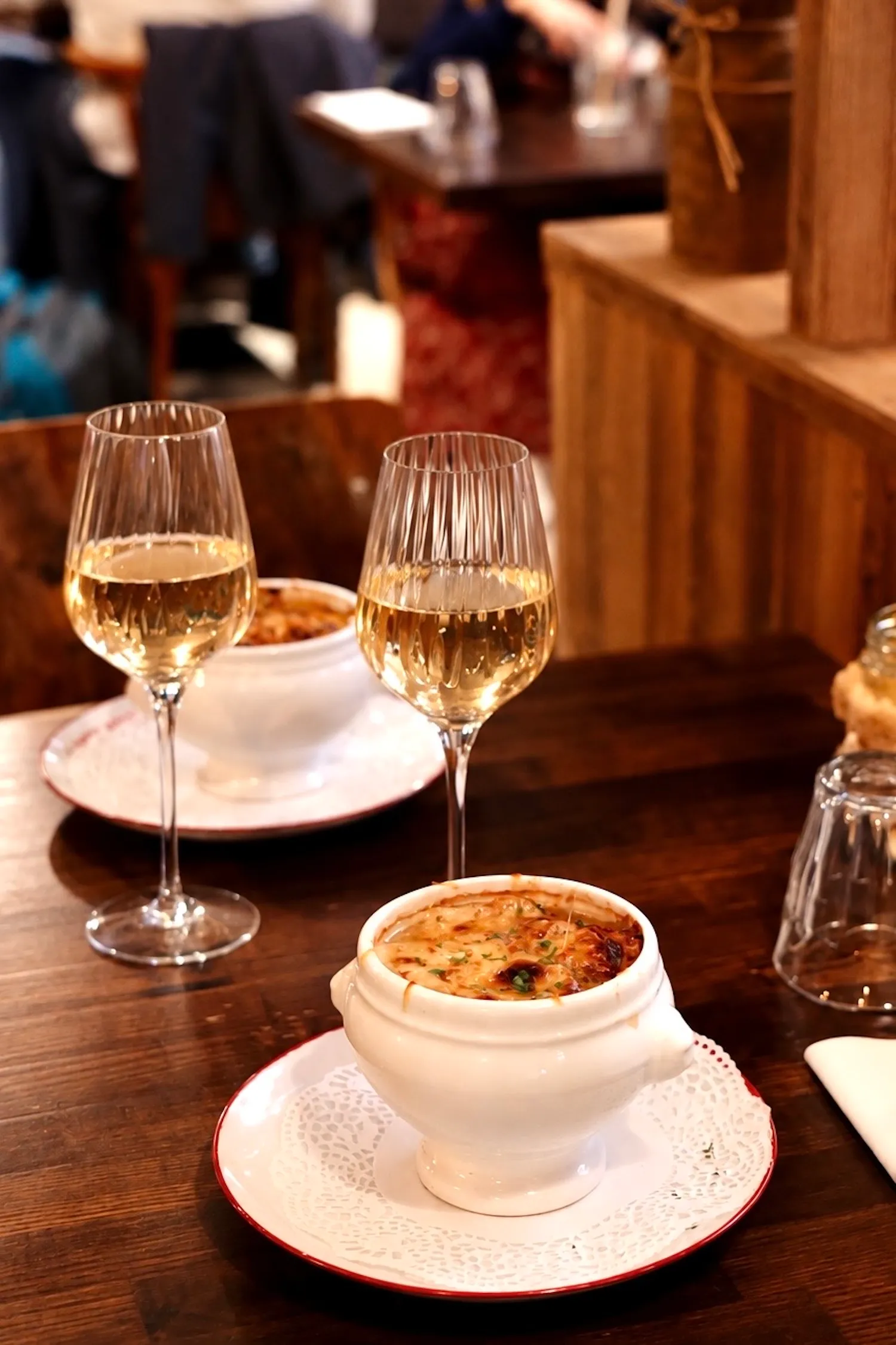 Soupe à l'oignon gratinée servie dans une soupière blanche, avec deux verres de vin blanc