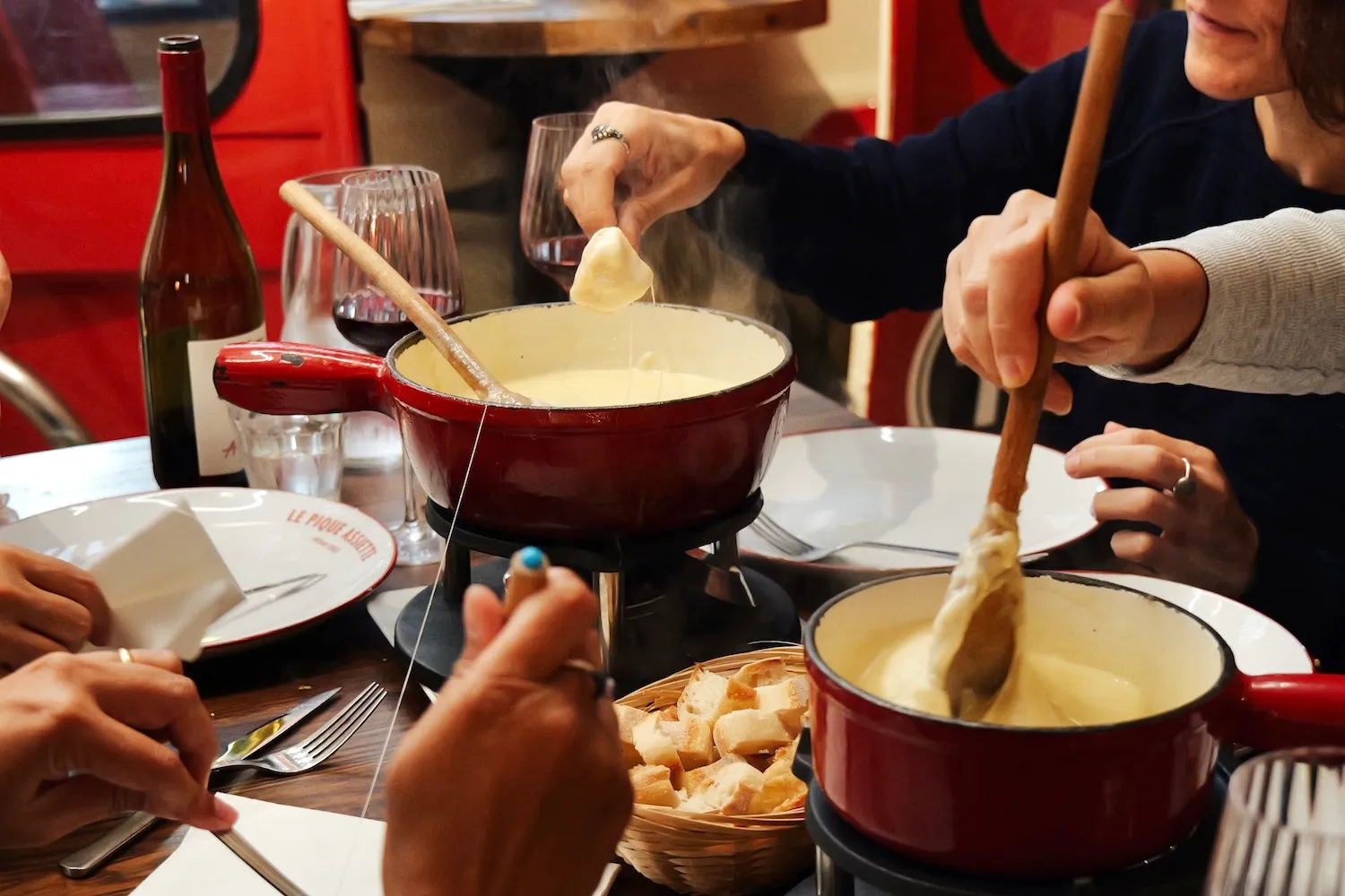 Fondue savoyarde fumante dans un caquelon rouge, avec panier de pain et bouteille de vin
