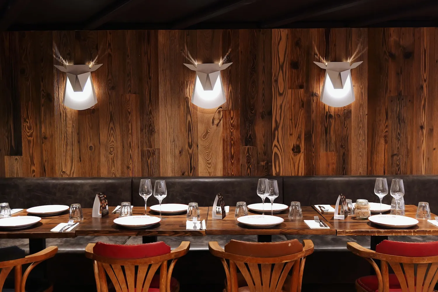 Mur en bois vieilli orné de trois lampes tête de cerf, au-dessus d'une longue table dressée