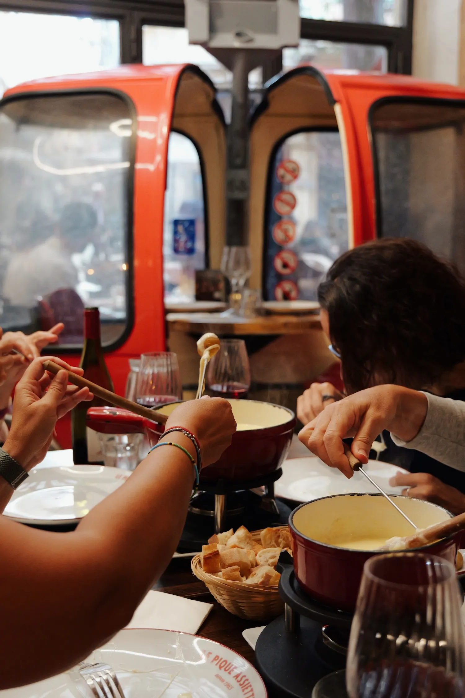 Convives dégustant une fondue savoyarde devant les cabines de télécabine rouges du Pique Assiette