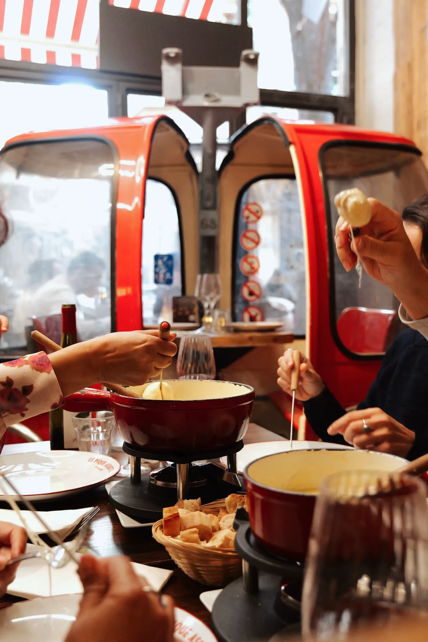 Fondue savoyarde partagée à table devant une cabine de télécabine rouge, repas de groupe au Pique Assiette