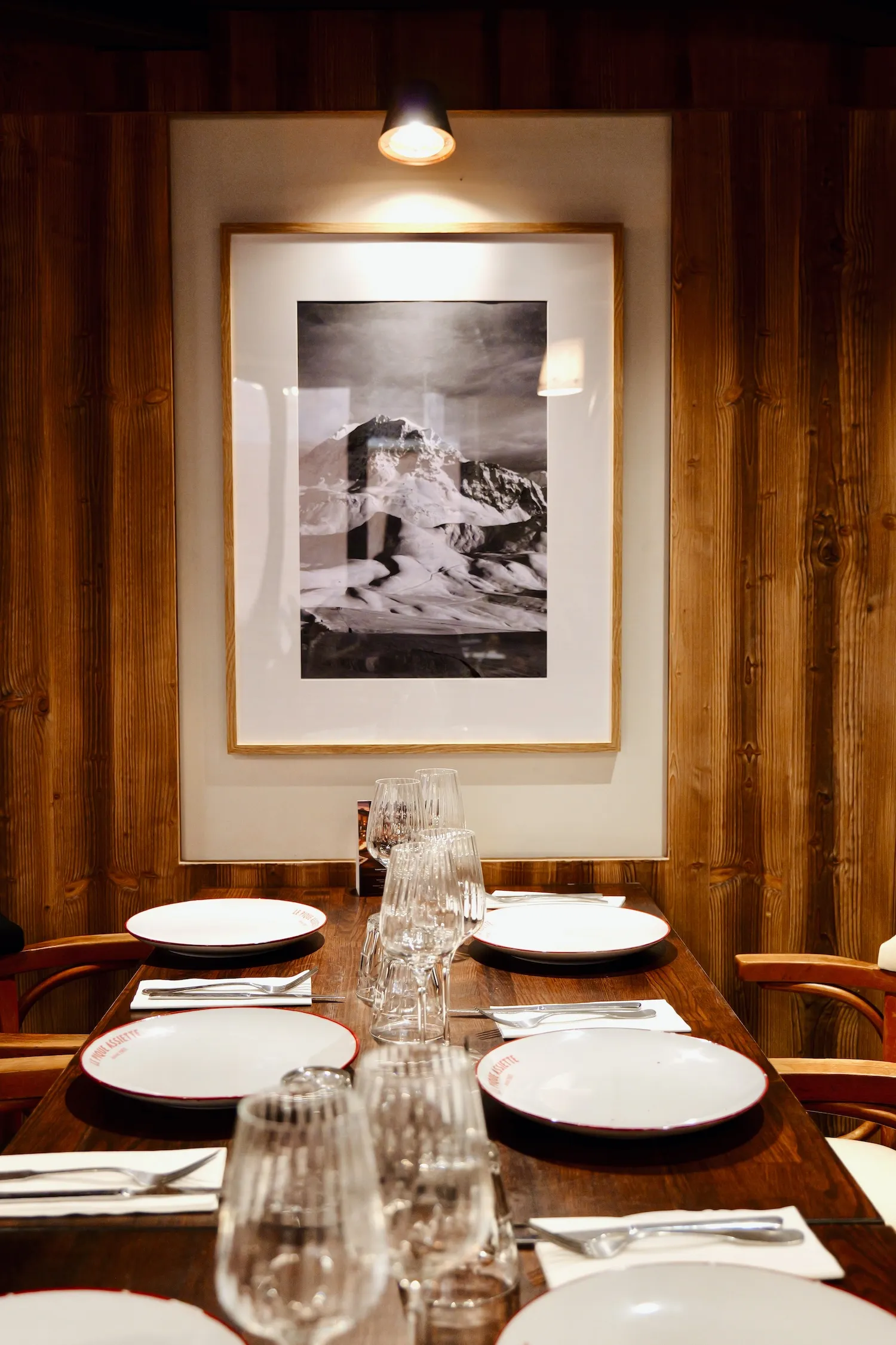 Table dressée devant un grand cadre noir et blanc de montagne, restaurant savoyard Le Pique Assiette