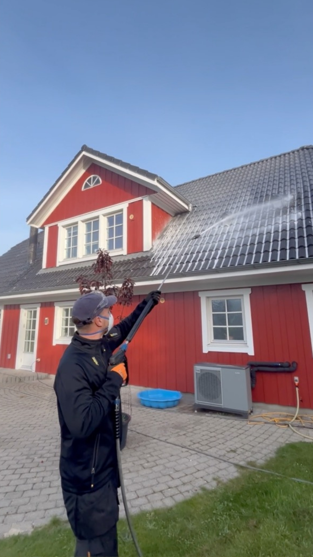 Person i lift sprøjter vand mod en bygning med røde mursten og rødt tegltag under en klar blå himmel.