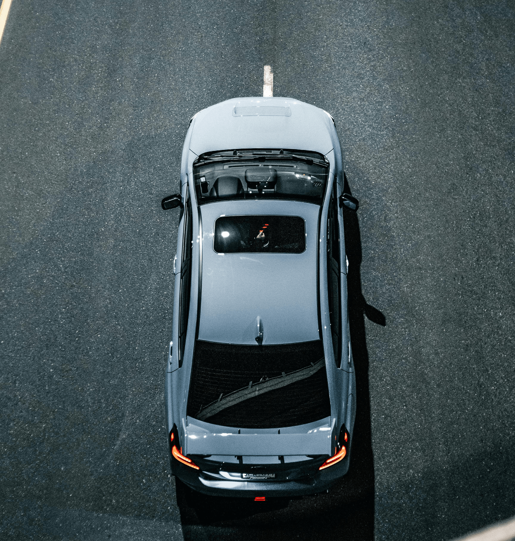 Top view of a silver car with tail lights on driving on a dark paved road.