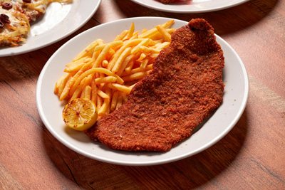 Plate with breaded fried schnitzel, French fries, and a grilled lemon half on a wooden table.