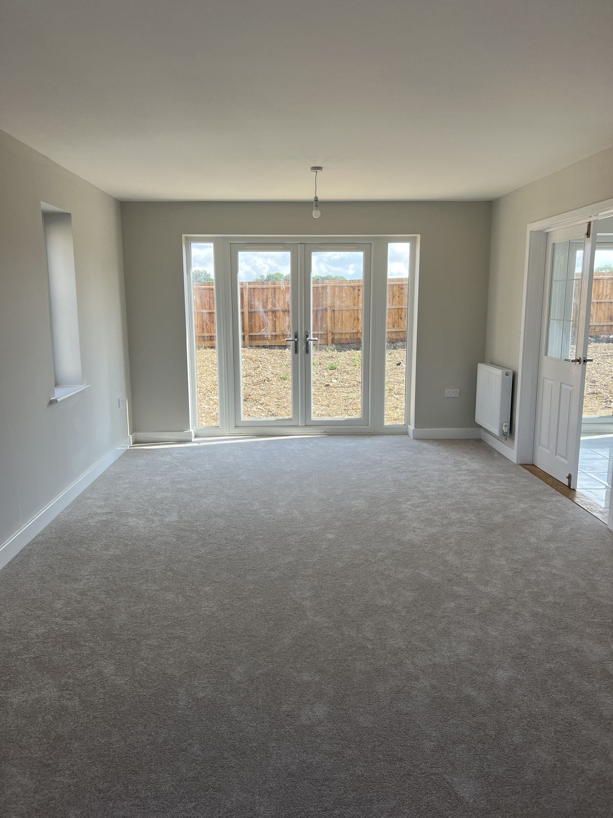 Empty room with gray carpet, beige walls, glass double doors, and a door to a tiled area.