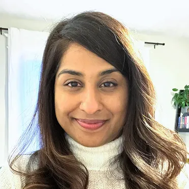 Smiling woman with long dark hair wearing a white turtleneck sweater indoors.